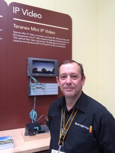 Simon Westland stands in front of the IP-transmission demo area, where a Teranex Mini IP video converter connects SD, HD, and UHD SDI equipment into an IP video-based broadcast infrastructure via a 10G optical-fiber data connection.